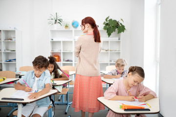 Fototapeta premium Teacher walking between desks while children writing test