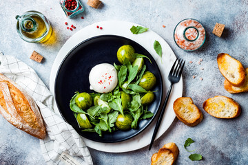 Green zebra tomatoes and burrata cheese salad with fresh arugula, olive oil and toasted bread. Overhead view