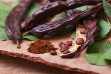 Carob. Organic carob pods with seeds and leaves on tree bark table. Healthy eating, food background.
