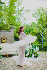 Seductive young bride in white negligee posing with big piece of white fabric