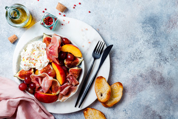 Summer fruit salad with burrata, peaches, figs, grapes, jamon or prosciutto and toasted bread. Top view, overhead