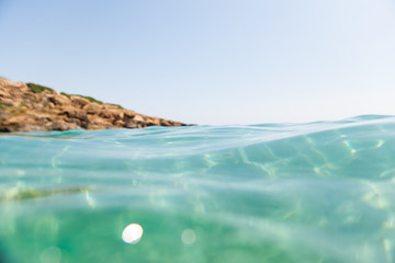 Turquoise blue sea above water surface and underwater. Sun glare at the bottom of ocean. Waves...