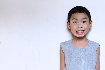 Asian black hair naughty boy age 5 years old wear gray t-shirt use baby powder on his face and say cheese for smiling with white cement wall background.