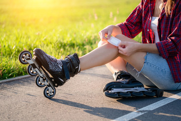 Woman injured knee while rollerblading. A teenager sticks a bruise with a band aid after falling...