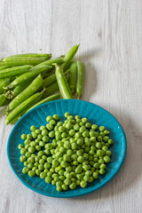 Garden peas with pods on a blue plate.  Grey wood background