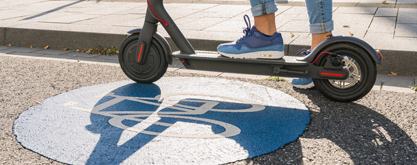 Close up of woman standing on a electric scooter or kick scooter at a blue Bicycle road sign