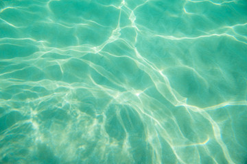 Fototapeta na wymiar Underwater. Sun glare at the bottom of the seat. Waves underwater and rays of sunlight shining through. Deep turquoise blue sea. Ocean. Transparent water and light at sand.