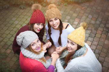 Girls in warm knitted clothes and hats hug, top view. Autumn day, a group of friends.