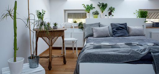 Modern and cozy interior of bedroom in scandinavian style. Plants as a decor indoors. Panorama.