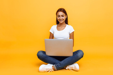 young woman sitting cross-legged using laptop isolated on yellow background