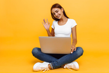 Young beautiful girl with a laptop, talking on Skype, on a yellow background