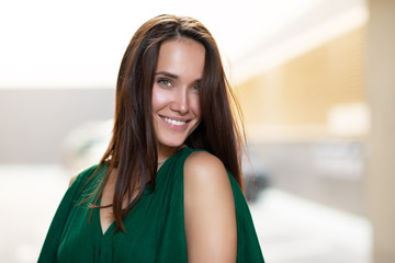 Young pretty likable cheerful woman posing summer city outdoor. Beautiful self-confident girl dressed in emerald-colored jumpsuit with long brown hair walking street enjoing her life, urban lifestyle