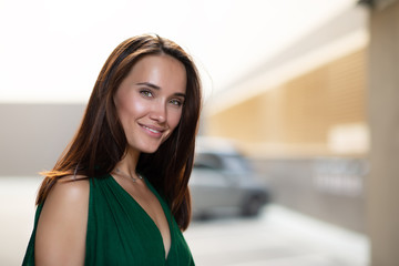 Young pretty likable cheerful woman posing summer city outdoor. Beautiful self-confident girl dressed in emerald-colored jumpsuit with long brown hair walking street enjoing her life, urban lifestyle