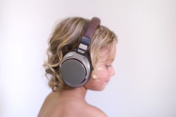 Fototapeta premium Happy smiling little child enjoys listens to music in headphones.Cute blond kid boy 4 years old on white background. People childhood lifestyle concept.Vivid and fun emotions. side view.