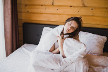Young woman having good morning in bed in cozy wooden house.