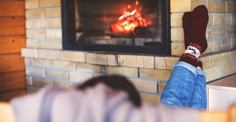 Woman relaxing with cup of tea near fireplace in cozy house.
