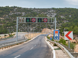 Asphalt road with many road signs and metal arch with direction arrows and speed limit signs