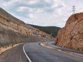 Asphalt road curves between two rock cliffs with openwork power line pillars atop