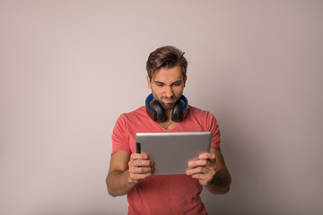 Young man having an exciting online game via portable touch pad computer while standing isolated in studio against grey wall with copy space background for promotional content