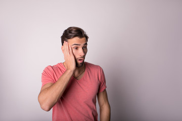 Young man shocked by bad news hold hands on face and looking in space background for promotional content.