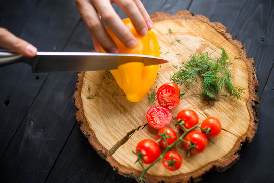 Chef cook cuts yellow bell pepper on a wooden board, closeup.