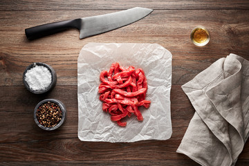 Chopped raw veal meat for beef stroganoff on white cooking paper and wooden table