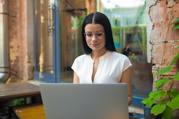 Woman intelligent business internet owner online banking via laptop computer while resting in restaurant. Female in glasses skilled writer having webinar via notebook, relaxing in coffee shop