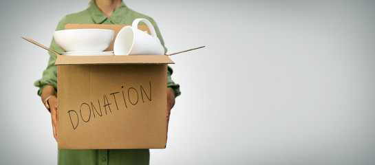 woman holding box with household items for donations on gray background with copy space - obrazy, fototapety, plakaty