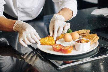 Close-up of male chef in protective gloves decorating his dish before serving at the restaurant