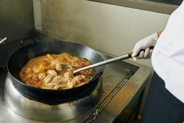 Close-up of chef standing near the stove and frying the meat on the pan in the kitchen
