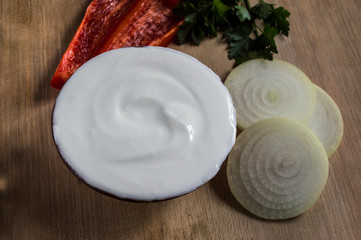plate with sour cream, paprika slices, parsley, onion rings on a wooden board