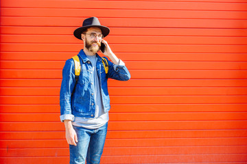 young handsome bearded hipster man using smartphone and listening music with earphones in the city,...
