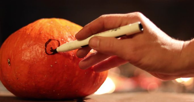 Halloween Hand draws a scary face on a pumpkin. fire in the background