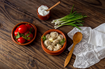 Boiled dumplings in a bowl, sour cream and pickled tomatoes close-up (russian and ukrainian cuisine)
