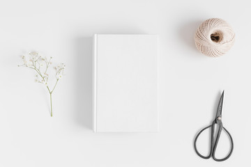 Top view of a book mockup with a gypsophila  and workspace accessories on a white table.