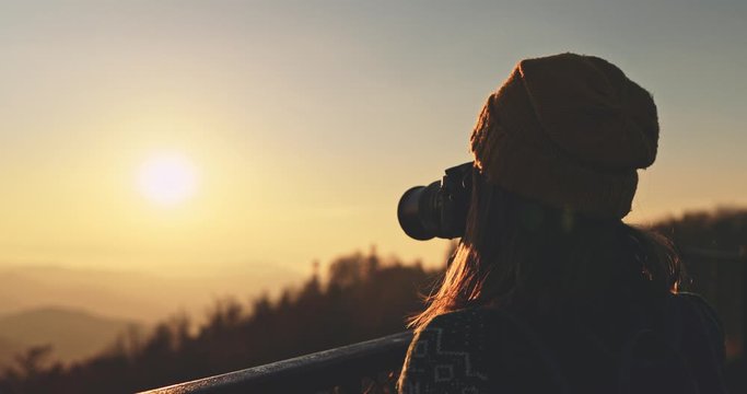 Young Woman Taking Pictures of Sunlit Fall Mountain Landscape form the Top. SLOW MOTION. Hiker Girl is Taking photos with digital camera of beautiful autumn hills landscape at sunset, Lens Flare.  
