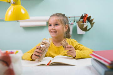 school girl eating biscuits, while doing homework in her room