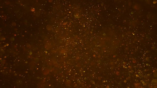 Gold bokeh bubbles and small glittering dust particles moving smoothly up and down on the dark background.
