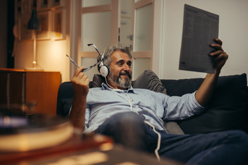 middle aged man sitting sofa and listening music on record player in his home
