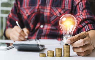 Business man holding light bulb and some coins on table writing  saving bank and account for his money all in finance accounting concept.