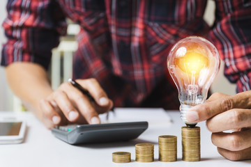 Business man holding light bulb and some coins on table writing  saving bank and account for his money all in finance accounting concept.