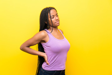 African American teenager girl with long braided hair over isolated yellow wall suffering from backache for having made an effort