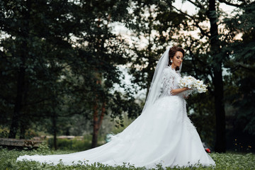 Fototapeta premium Bride holding a bouquet of white orchids. Beautiful woman. Wedding bouquet in bride's hands. Beautiful bride in white dress in the garden. Beautiful woman with professional make up and hair style.