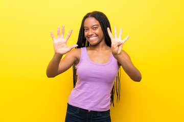 African American teenager girl with long braided hair over isolated yellow wall counting nine with...