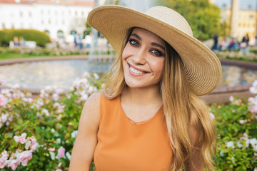Portrait of a happy smiling gorgeous European female in fashionable wicker hat looking in camera while sitting outdoors in summer day during leisure time in weekend