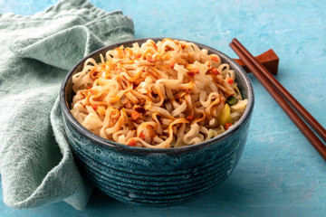 Instant ramen noodles with carrot and a sauce, a close-up with chopsticks on a blue background