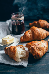 croissants, plum jam and butter on dark wooden table with copyspace