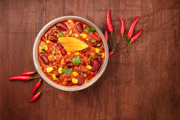 Chili con carne, traditional Mexican dish, shot from the top on a dark rustic wooden background with a nacho chip, red chilli peppers, and a place for text
