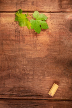 A design template for a wine menu or tasting invitation. A vine leaf and a wine cork, shot from the top on a dark rustic wooden background with a place for text