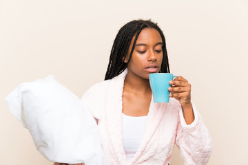 African American teenager girl with long braided hair in pajamas over isolated background and holding a cup of coffee